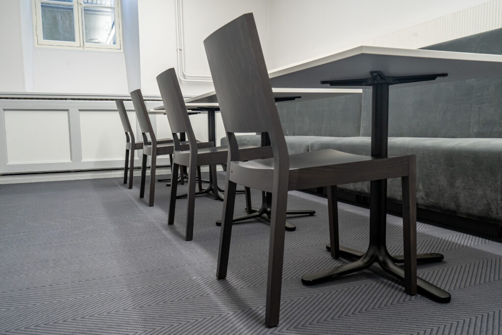 Hallis puhkeruumis reas olevad tumedad toolid valgete laudade ääres.